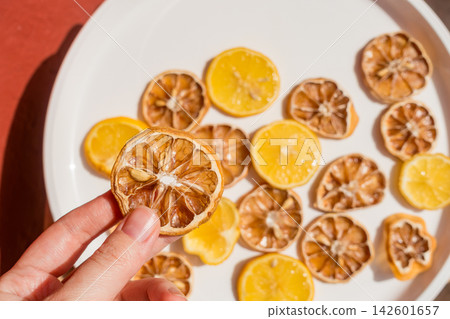 Hand Holding a Dried Lemon Slice Over a Plate of Fresh and Dried Lemon Slices Hand Holding a Dried Lemon Slice Over a Plate of Fresh and Dried Lemon Slices 142601657