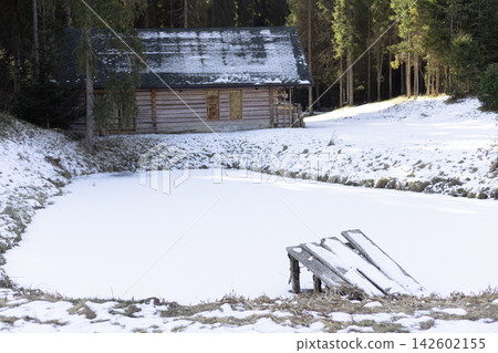 Wooden cabin by frozen pond in snowy forest Wooden cabin by frozen pond in snowy forest 142602155