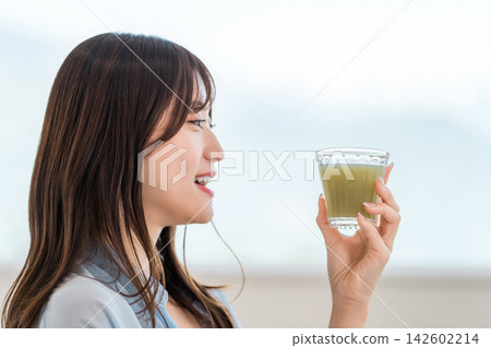 一位年輕女子早餐喝一杯綠色蔬果。這是她注重營養健康的晨間習慣。 142602214