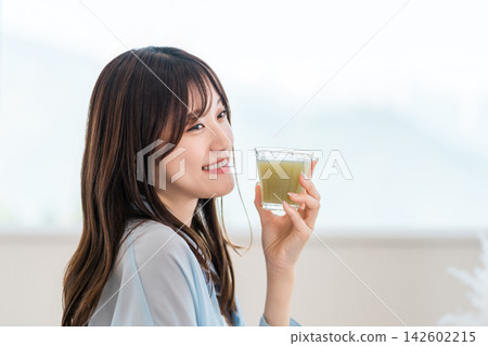 A young woman drinks a green smoothie for breakfast. A morning habit focused on nutrition and health. A young woman drinks a green smoothie for breakfast. A morning habit focused on nutrition and health. 142602215