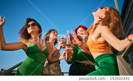 Female friends celebrate with beer while dancing in bright summer sunshine Female friends celebrate with beer while dancing in bright summer sunshine 142602842