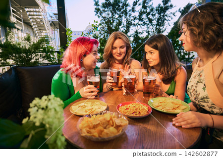 Smiling friends hold beer glasses above table with pizza and crunchy snacks Smiling friends hold beer glasses above table with pizza and crunchy snacks 142602877