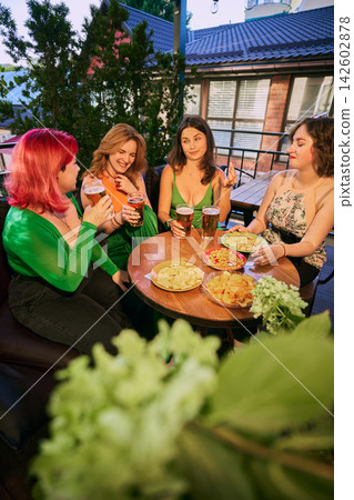 Group of women gather around beer and snacks at cozy outdoor restaurant Group of women gather around beer and snacks at cozy outdoor restaurant 142602878