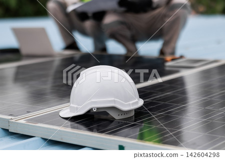 White safety helmet resting on solar panels during outdoor installation, with a blurred worker in the background. White safety helmet resting on solar panels during outdoor installation, with a blurred worker in the background. 142604298