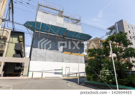 一棟正在施工的建築物,被臨時圍欄和鷹架覆蓋。 一棟正在施工的建築物,被臨時圍欄和鷹架覆蓋。 142604483