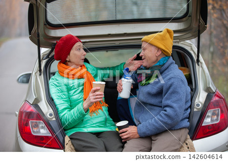 An elderly couple shares warm moments in the backseat of a car on an autumn day in a natural setting. An elderly couple shares warm moments in the backseat of a car on an autumn day in a natural setting. 142604614