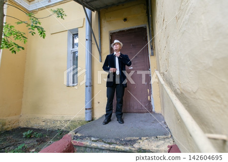 Man in formal attire stands thoughtfully near a weathered building entrance on a calm day 142604695