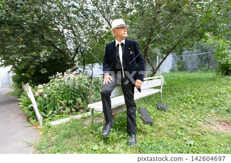 Man in seersucker suit and hat poses on bench in lush garden during sunny day Man in seersucker suit and hat poses on bench in lush garden during sunny day 142604697