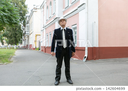 Senior man dressed in formal attire stands confidently in urban alley during daytime surrounded by buildings Senior man dressed in formal attire stands confidently in urban alley during daytime surrounded by buildings 142604699