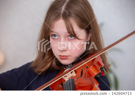 Young girl plays violin with focus during music practice in a bright room Young girl plays violin with focus during music practice in a bright room 142604715
