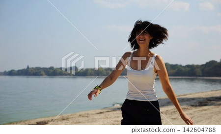 Beautiful lady walking on sandy beach near shoreline at sunny day. Happy adult woman turning around near coastline. Carefree female enjoying rest at seaside. Concept of summer vacation or holiday Beautiful lady walking on sandy beach near shoreline at sunny day. Happy adult woman turning around near coastline. Carefree female enjoying rest at seaside. Concept of summer vacation or holiday 142604788