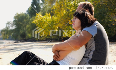 Happy pair hugs during sitting on wooden log on beach. Romantic couple admiring sea landscape at sunny day. Lovers spending time together at resort. Concept of summer vacation or holiday. Slow mo Happy pair hugs during sitting on wooden log on beach. Romantic couple admiring sea landscape at sunny day. Lovers spending time together at resort. Concept of summer vacation or holiday. Slow mo 142604789