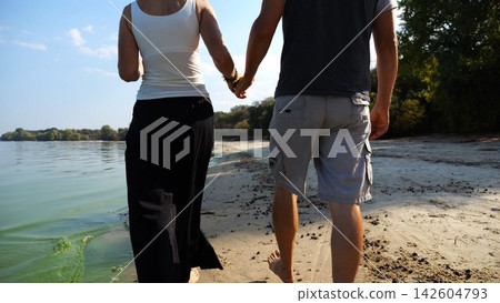 Romantic couple holding hands of each other and walking at coastline. Happy pair going along seashore at sunny day. Lovers spending time together at resort. Concept of vacation or holiday. Slow motion Romantic couple holding hands of each other and walking at coastline. Happy pair going along seashore at sunny day. Lovers spending time together at resort. Concept of vacation or holiday. Slow motion 142604793