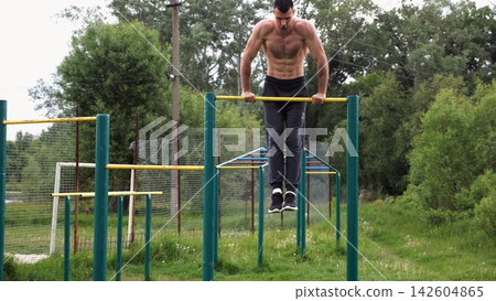 Hardy shirtless sportsman doing push ups on horizontal bar at nature. Strong and muscular guy training at sports ground. Young athletic guy exercising outdoor. Concept of active and healthy lifestyle Hardy shirtless sportsman doing push ups on horizontal bar at nature. Strong and muscular guy training at sports ground. Young athletic guy exercising outdoor. Concept of active and healthy lifestyle 142604865