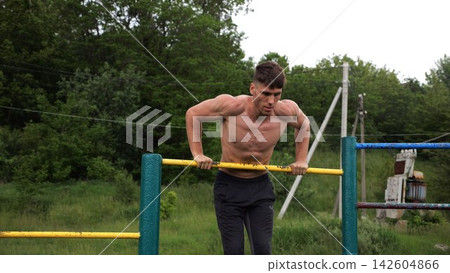 Hardy shirtless sportsman doing push ups on horizontal bar at nature. Strong and muscular guy training at sports ground. Young athletic guy exercising outdoor. Concept of active and healthy lifestyle Hardy shirtless sportsman doing push ups on horizontal bar at nature. Strong and muscular guy training at sports ground. Young athletic guy exercising outdoor. Concept of active and healthy lifestyle 142604866