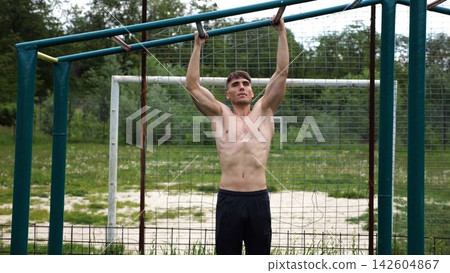 Young muscular sportsman doing pull ups at sports ground. Athletic guy exercising outdoor. Strong sporty man working out at summer nature. Concept of healthy and active lifestyle. Slow motion Young muscular sportsman doing pull ups at sports ground. Athletic guy exercising outdoor. Strong sporty man working out at summer nature. Concept of healthy and active lifestyle. Slow motion 142604867