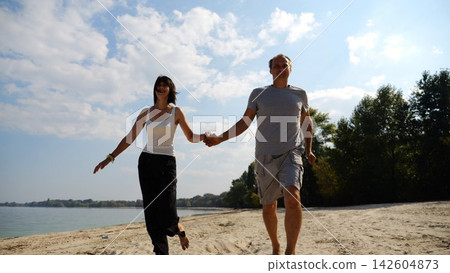 Romantic couple holding hands of each other and jogging at coastal. Happy pair running along seashore at sunny day. Lovers spending time together at resort. Concept of summer vacation or holiday Romantic couple holding hands of each other and jogging at coastal. Happy pair running along seashore at sunny day. Lovers spending time together at resort. Concept of summer vacation or holiday 142604873