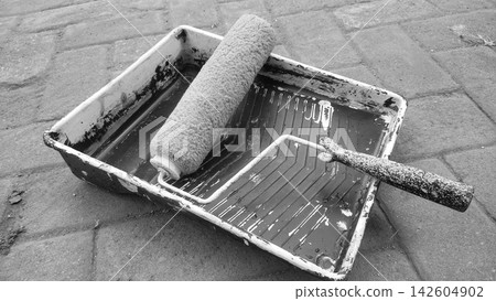 Monochrome Image of Paint Roller and Tray Resting on Paved Ground Monochrome Image of Paint Roller and Tray Resting on Paved Ground 142604902