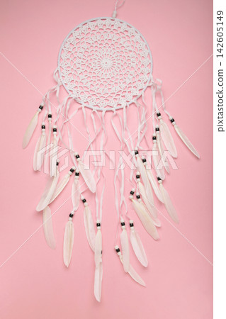 Handmade dream catcher hanging on a rope with feathers, threads, and beads on pink background. Handmade dream catcher hanging on a rope with feathers, threads, and beads on pink background. 142605149