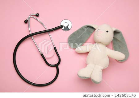 Pediatrician concept. Toy bunny and stethoscope on pink background. Pediatrician concept. Toy bunny and stethoscope on pink background. 142605170