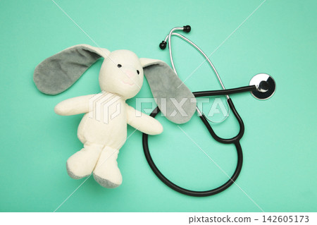 Pediatrician concept. Toy bunny and stethoscope on mint background. Pediatrician concept. Toy bunny and stethoscope on mint background. 142605173