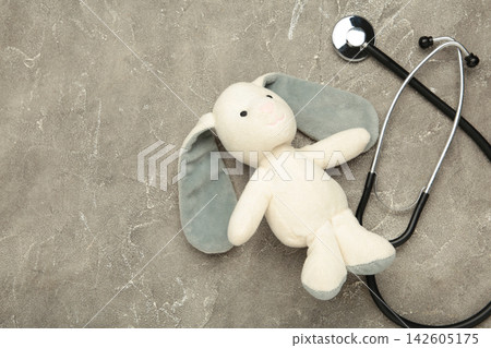 Pediatrician concept. Toy bunny and stethoscope on grey concrete background. Pediatrician concept. Toy bunny and stethoscope on grey concrete background. 142605175