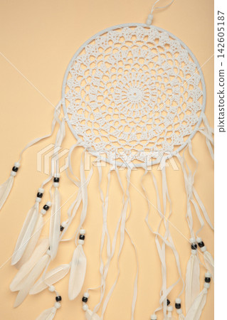 Handmade dream catcher hanging on a rope with feathers, threads, and beads on beige background. Handmade dream catcher hanging on a rope with feathers, threads, and beads on beige background. 142605187
