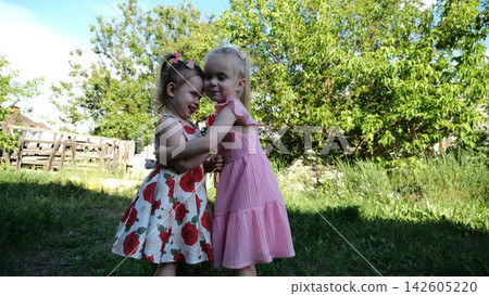 Two cute little sisters hugging each other tightly on green grass outdoor. Beautiful small girls smiling and embracing in summer garden on sunny day. Carefree children show family love and friendship Two cute little sisters hugging each other tightly on green grass outdoor. Beautiful small girls smiling and embracing in summer garden on sunny day. Carefree children show family love and friendship 142605220