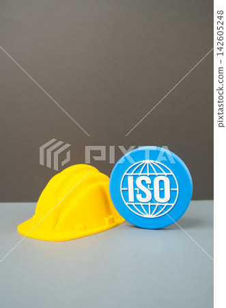 Construction helmet and ISO symbol, quality standards in construction concept. Building regulations, certification, safety compliance and professional requirements for reliable infrastructure Construction helmet and ISO symbol, quality standards in construction concept. Building regulations, certification, safety compliance and professional requirements for reliable infrastructure 142605248