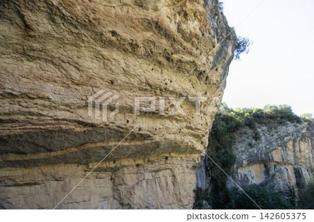 Layered limestone rock overhang and shelter seen from below against a bright sky Layered limestone rock overhang and shelter seen from below against a bright sky 142605375