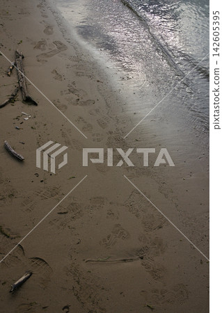 海浪拍打著沙灘,還有漂浮的木頭和腳印。 海浪拍打著沙灘,還有漂浮的木頭和腳印。 142605395