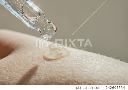 Clear cosmetic serum dropping from pipette onto dry human skin, providing hydration Clear cosmetic serum dropping from pipette onto dry human skin, providing hydration 142605534
