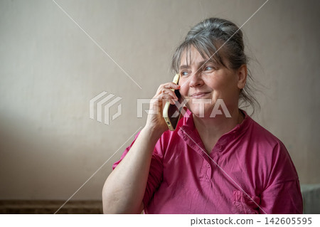 Mature woman speaking on smartphone at home against a neutral wall. Menopause support telemedicine consultation and women's health communication 142605595