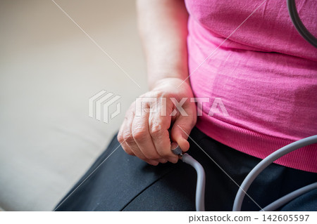 Midlife woman holding a blood pressure monitor tube while seated at home. Menopause health cardiovascular awareness and home monitoring 142605597