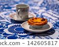 Close-up of pastel de nata custard tart with coffee cup on blue tablecloth on sunny day outdoors 142605817