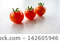 Three ripe cherry tomatoes with green stems arranged on clean white surface under soft natural light, vivid red produce with shallow depth and minimal food styling for fresh ingredient concepts 142605946