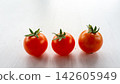 Three ripe cherry tomatoes with green stems arranged on bright white surface, isolated with soft natural light, fresh red color, clean minimal food composition for healthy cooking themes 142605949