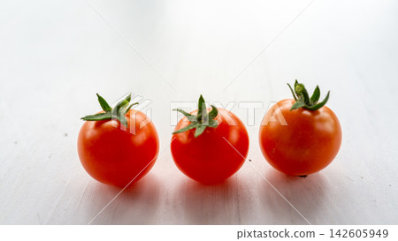 Three ripe cherry tomatoes with green stems arranged on bright white surface, isolated with soft natural light, fresh red color, clean minimal food composition for healthy cooking themes Three ripe cherry tomatoes with green stems arranged on bright white surface, isolated with soft natural light, fresh red color, clean minimal food composition for healthy cooking themes 142605949