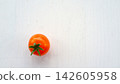 Single ripe red tomato with green stem on pale wooden surface in minimal overhead composition, fresh organic produce isolated in bright natural light with clean copy space 142605958