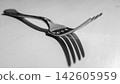 Close-up macro view of stainless steel fork on light neutral surface, with sharp prongs, reflective highlights, and dramatic shadow for dining, table setting, and minimal food concepts 142605959