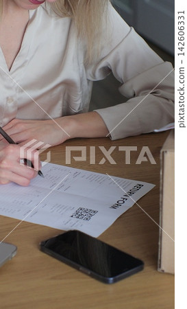 Vertical video. A person writes a return order and sits at a table with a laptop at home. Close-up of a customer writing on paper and filling out a form, wanting to return a product. Vertical video. A person writes a return order and sits at a table with a laptop at home. Close-up of a customer writing on paper and filling out a form, wanting to return a product. 142606331