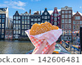 Hand Holds Bitten Stroopwafel Cookie in Front of Amsterdam Canal and Houses Netherlands 142606481