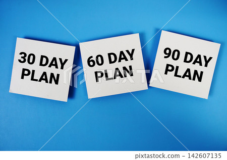 30 Day, 60 Day, 90 Day Plan message on paper note flat lay on blue background 30 Day, 60 Day, 90 Day Plan message on paper note flat lay on blue background 142607135