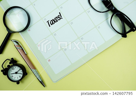 Taxes! message written on calendar date with alarm clock, glasses and magnifying glass on yellow background Taxes! message written on calendar date with alarm clock, glasses and magnifying glass on yellow background 142607795