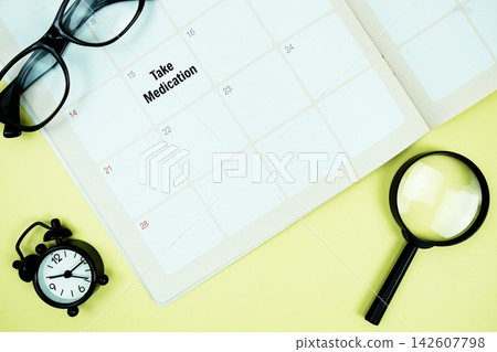 Take Medication message written on calendar date with alarm clock, glasses and magnifying glass on yellow background Take Medication message written on calendar date with alarm clock, glasses and magnifying glass on yellow background 142607798