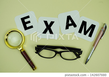 EXAM alphabet letters with magnifying glass, eye glasses and pen on yellow background EXAM alphabet letters with magnifying glass, eye glasses and pen on yellow background 142607880