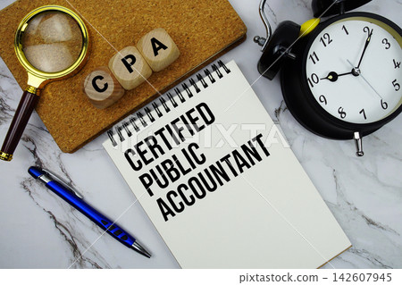 CPA Certified Public Accountant text written on notepad with magnifying glass and alarm clock on marble background CPA Certified Public Accountant text written on notepad with magnifying glass and alarm clock on marble background 142607945