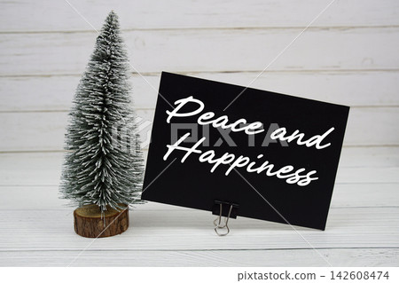 Peace and Happiness text written on paper card with snowy tree on wooden background Peace and Happiness text written on paper card with snowy tree on wooden background 142608474