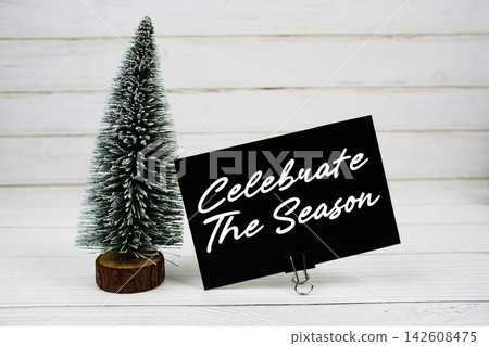 Celebrate the Season text written on paper card with snowy tree on wooden background Celebrate the Season text written on paper card with snowy tree on wooden background 142608475