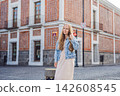 Woman tourist in a light dress and denim jacket walking through colorful colonial streets in Puebla Mexico with red brick building cobblestone road backpack solo female travel city break. 142608545